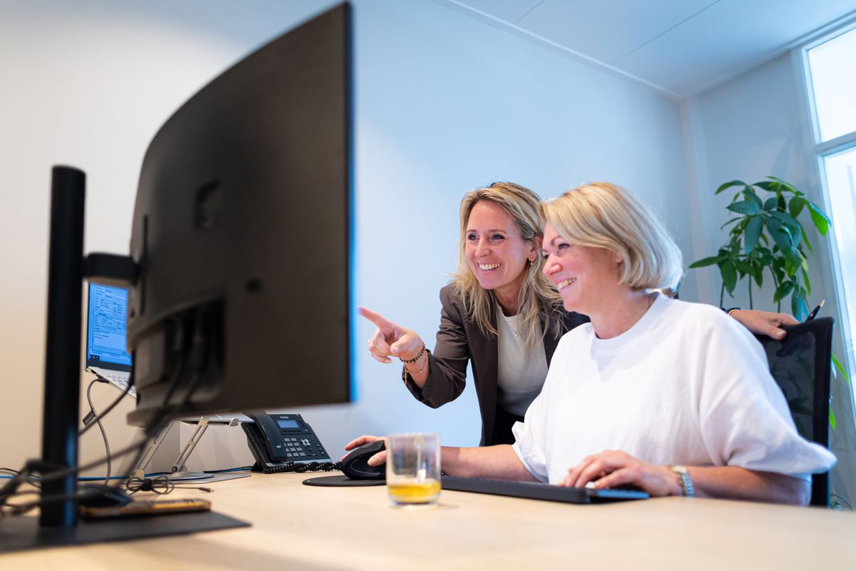 Laura en Hedwig kijken lachend samen naar een beeldscherm